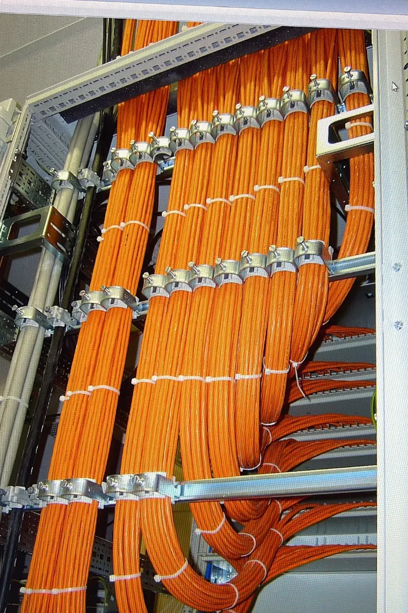 Dicke Bündel an orangen Netzwerkkabeln, die sicher an einer metallenen Kabeltrasse befestigt sind.